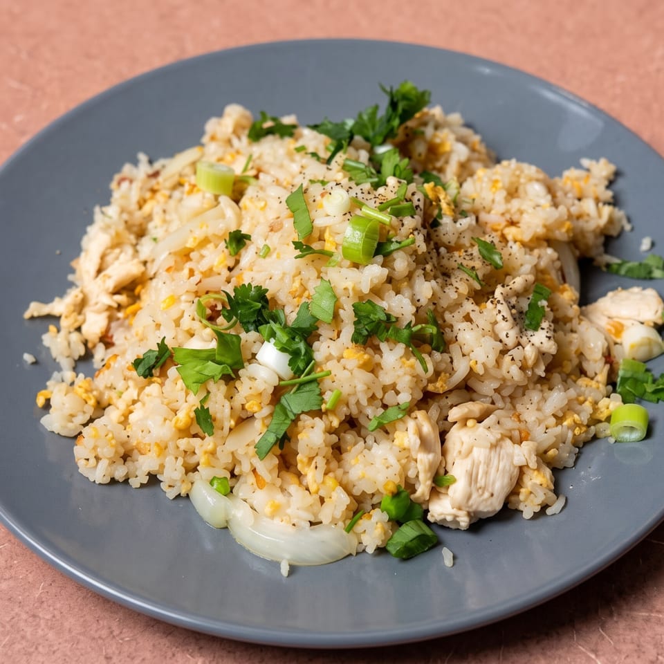 Chicken fried rice with scrambled egg, onions, and fresh herbs on a grey plate.