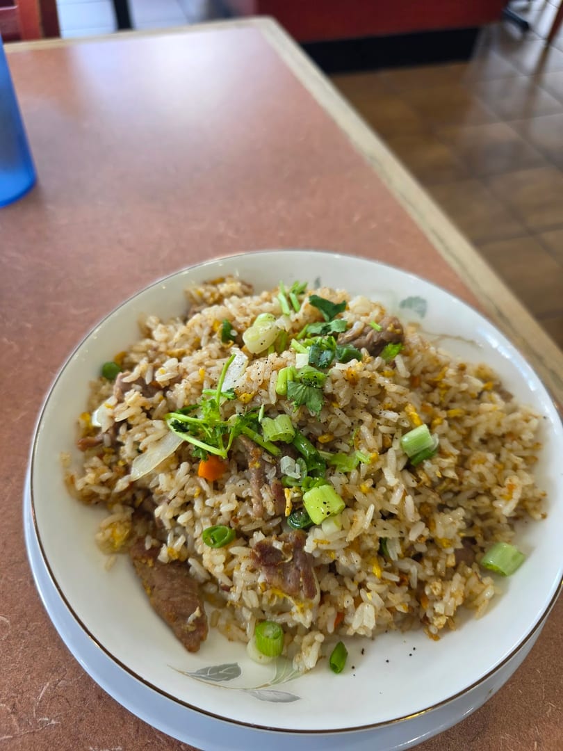 A plate of fried rice with beef, vegetables, and green onions on a brown table.