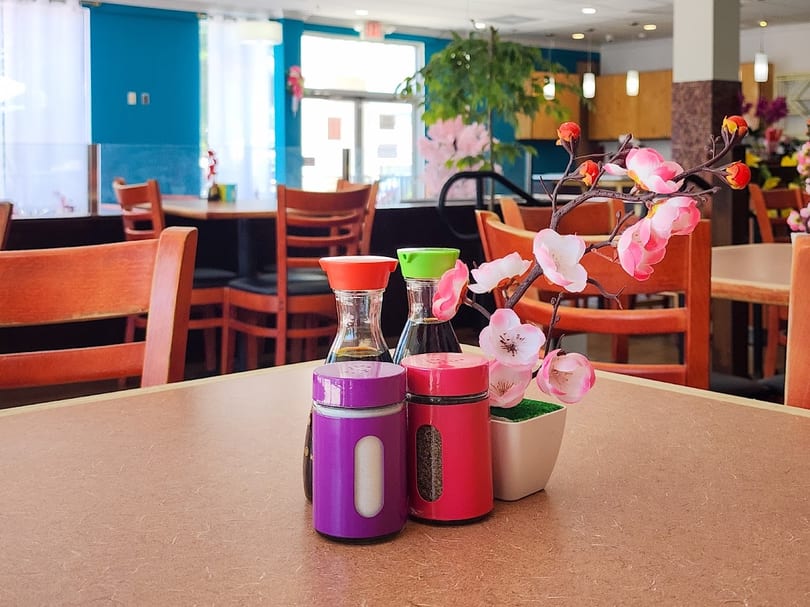 Table setting with soy sauce, shakers, and pink artificial flowers in a restaurant.
