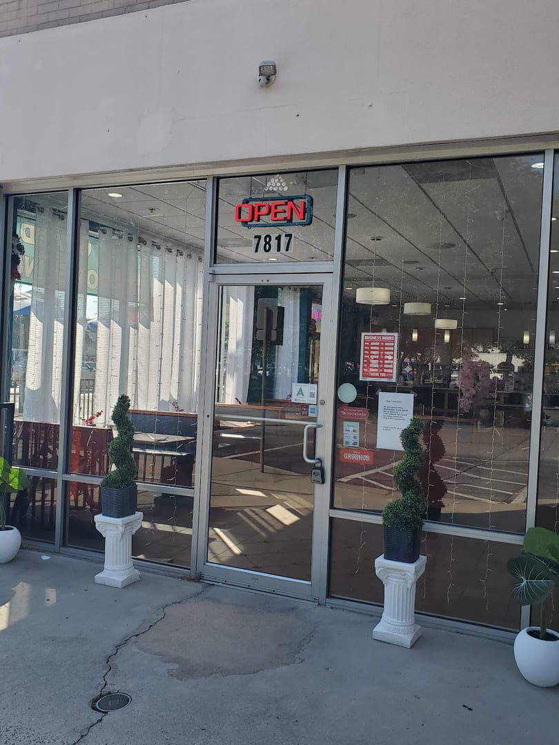 Exterior of a restaurant with a bright red "OPEN" sign and address 7817 above the glass door.