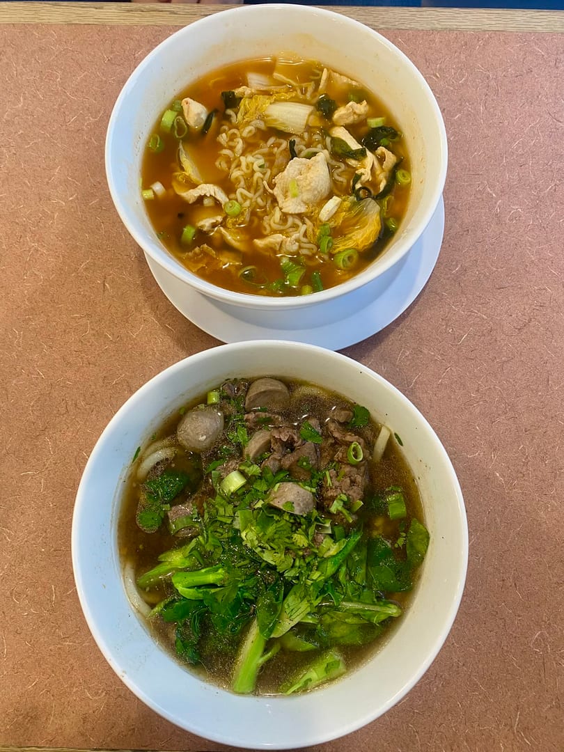 Two bowls of Asian noodle soup, one with ramen and chicken, the other with beef and greens.